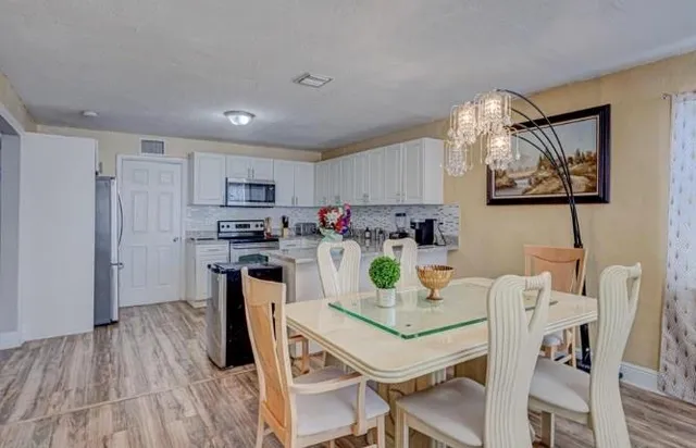 a kitchen with stainless steel appliances granite countertop a dining table chairs and refrigerator