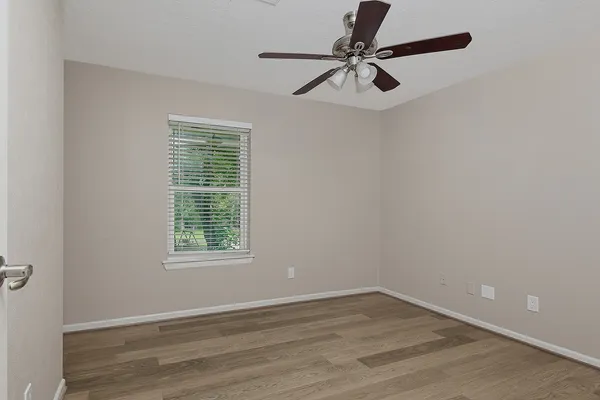 an empty room with wooden floor fan and windows