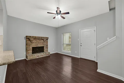 an empty room with wooden floor a ceiling fan a fireplace and windows