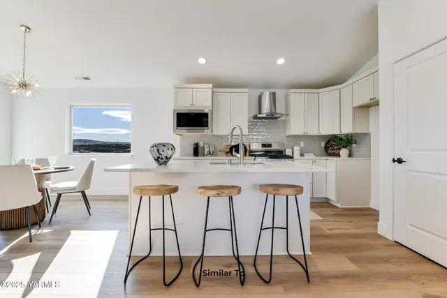 a kitchen with stainless steel appliances granite countertop a stove a sink a refrigerator and white cabinets with wooden floor