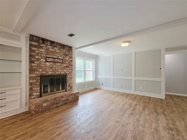 a view of an empty room with wooden floor fireplace and a window