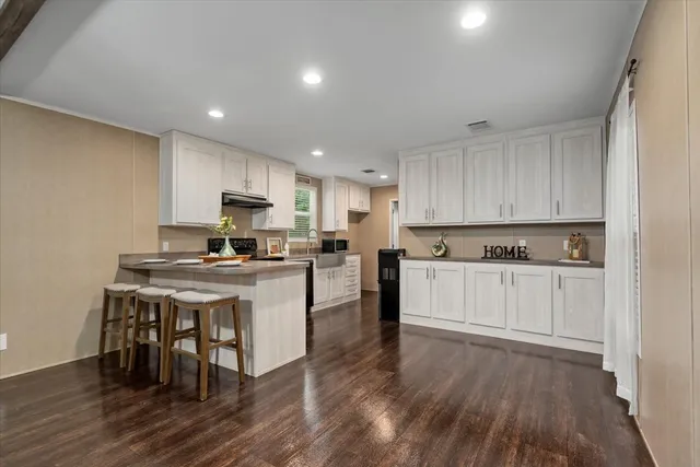 a kitchen with a sink a stove a refrigerator and white cabinets with wooden floor