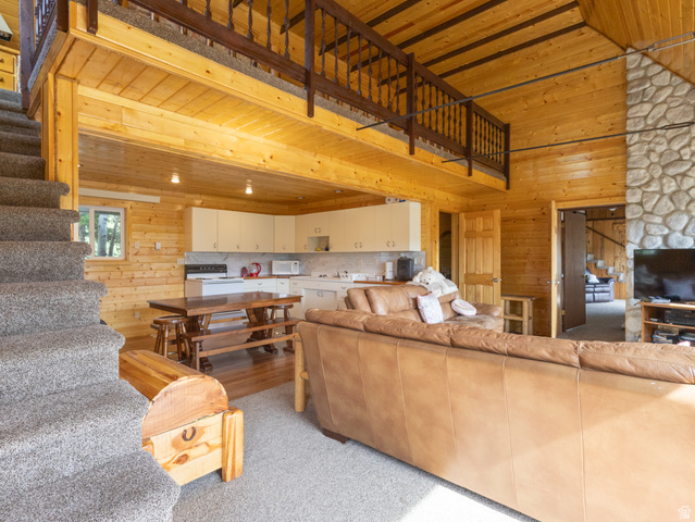 4770 Pine Crest Road Evanston, UT 82930 - Photo 10 of 24 Expansive open-concept living area featuring natural wood paneling throughout, a carpeted staircase leading to a loft space with wood railing, a stone-clad column, and a kitchen area with white cabinetry and a white subway tile backsplash