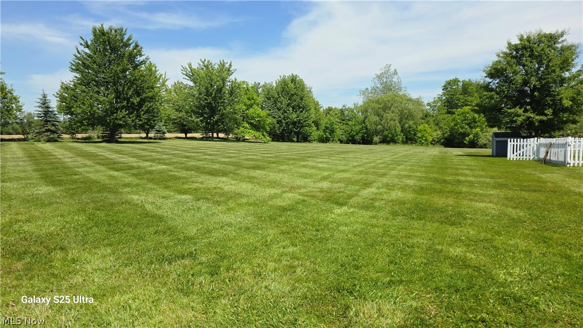 294 Twp 150 Road Sullivan, OH 44880 - Photo 35 of 39 Expansive green lawn with striped mowing pattern, mature perimeter trees, and a white picket fence partially enclosing a storage shed