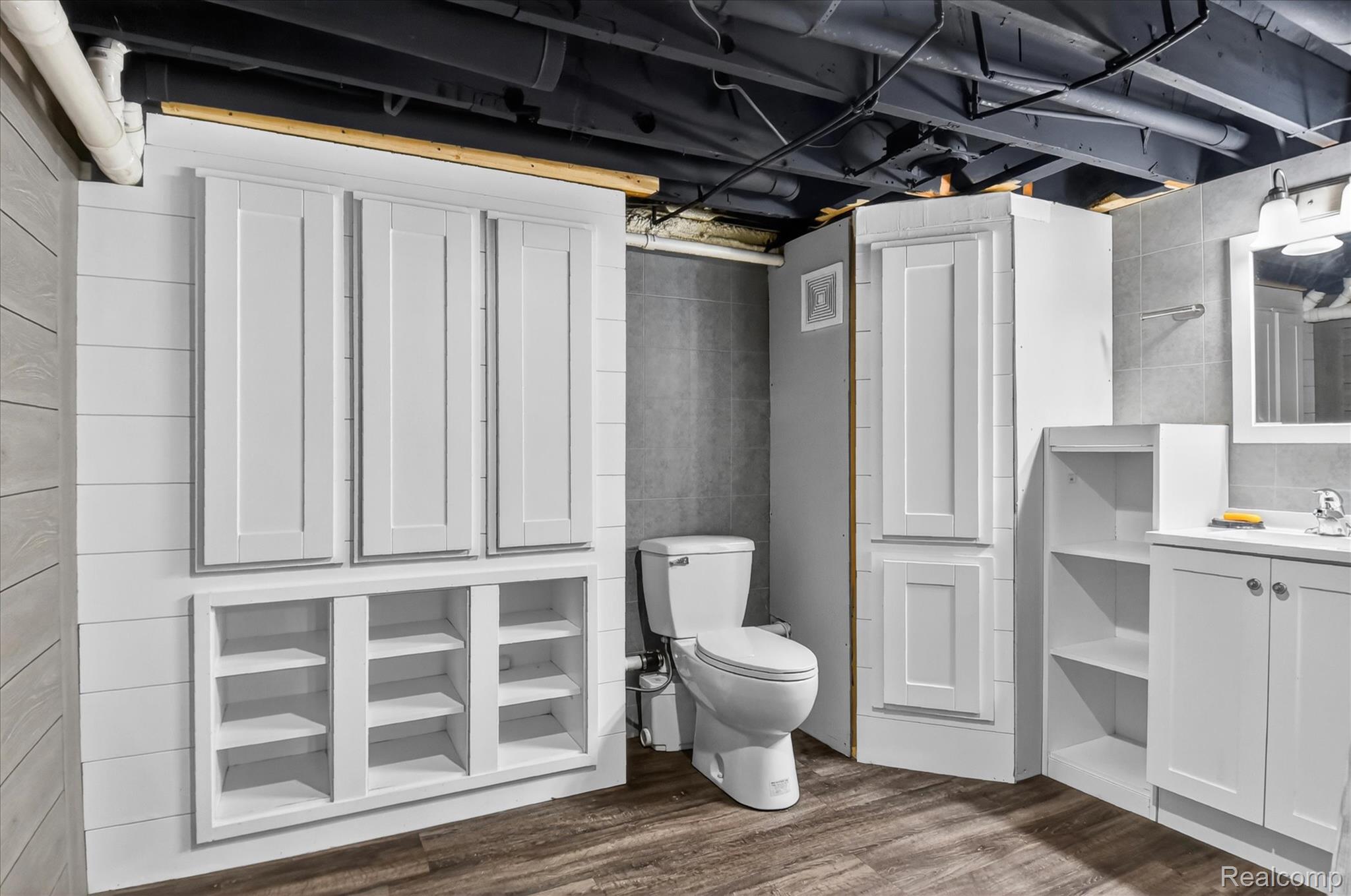 3949 West Burns Line Road Brown City, MI 48416 - Photo 53 of 70 Bathroom featuring wood-finish flooring, a white vanity with an undermount sink, a wall-mounted mirror, and a white toilet