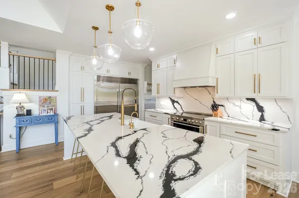 a kitchen with stainless steel appliances kitchen island granite countertop a sink dishwasher and white cabinets with wooden floor