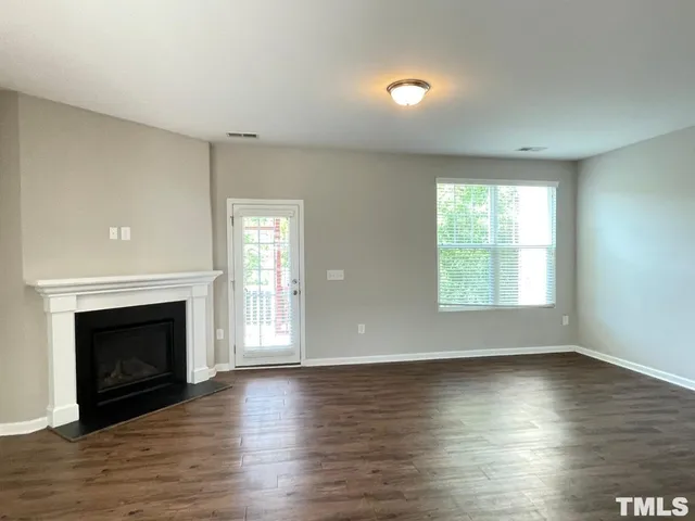 an empty room with wooden floor fireplace and windows