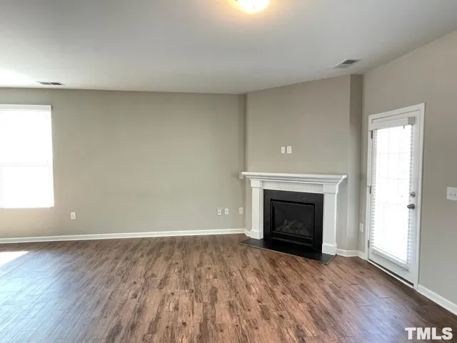 an empty room with wooden floor fireplace and windows