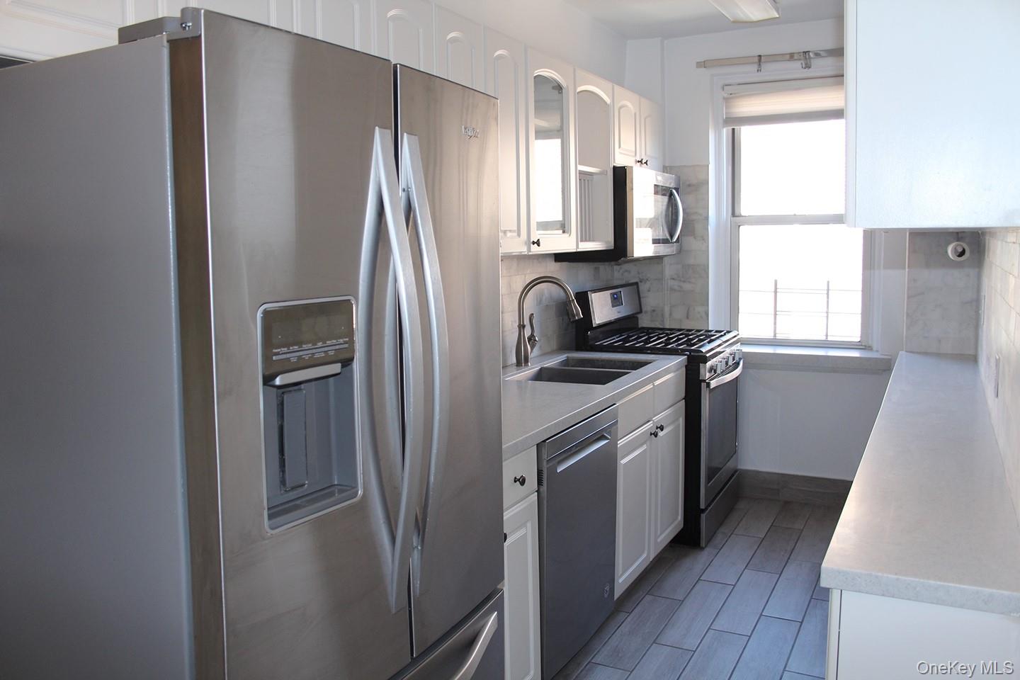 811 Bronx River Road, Unit 5A Yonkers, NY 10708 - Photo 2 of 18 Kitchen featuring appliances with stainless steel finishes, white cabinetry, light countertops, tasteful backsplash, and glass insert cabinets