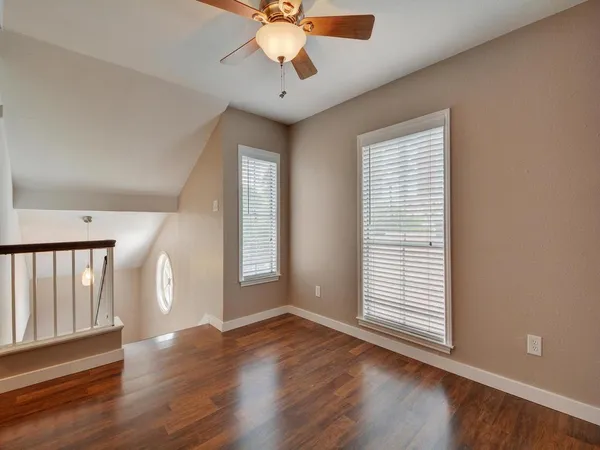 an empty room with wooden floor chandelier fan and windows