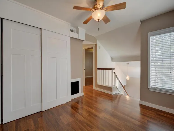 an empty room with wooden floor fan and windows