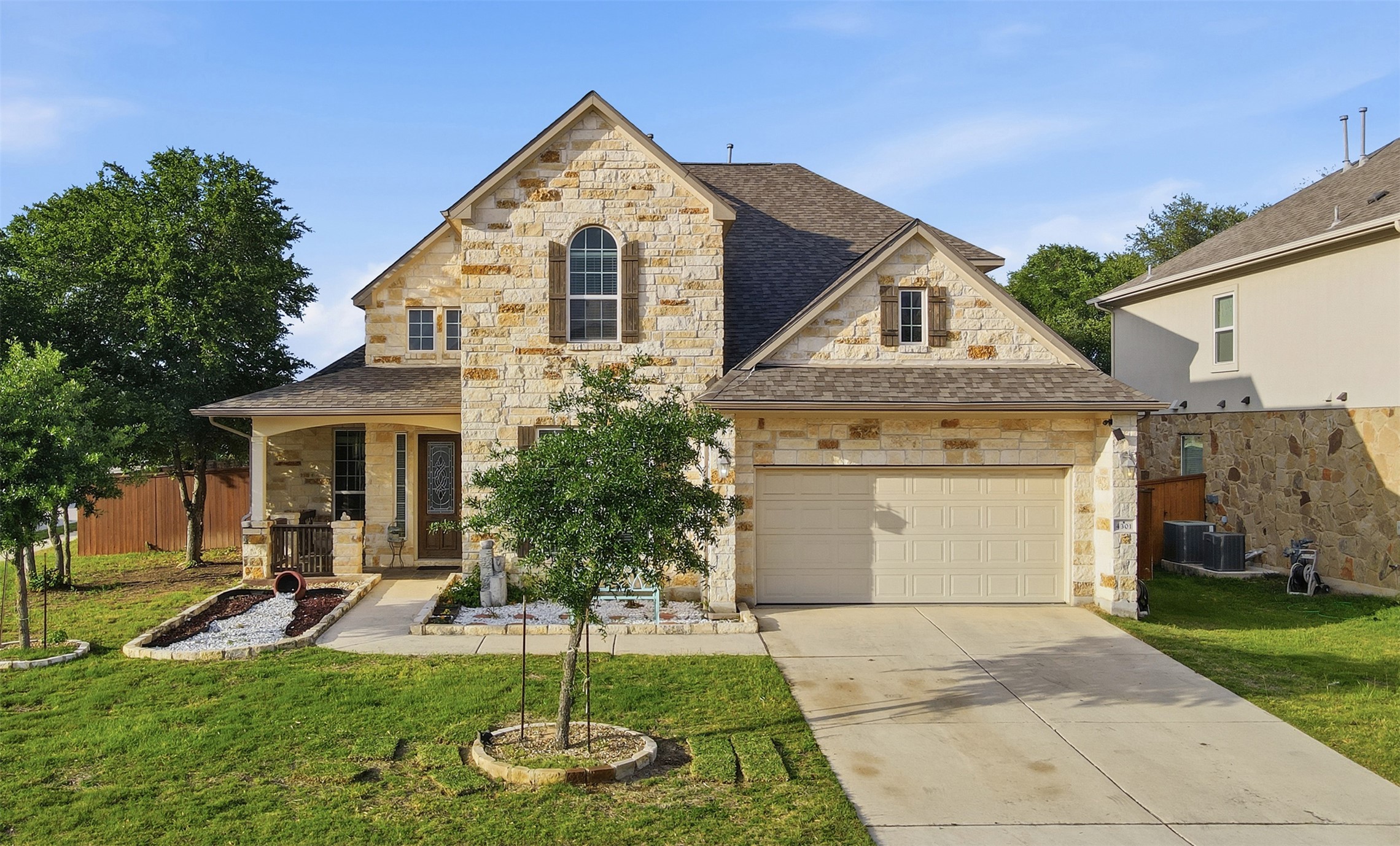 French country inspired facade featuring stone siding, a porch, driveway, and roof with shingles