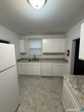 a kitchen with granite countertop a refrigerator a sink and white cabinets