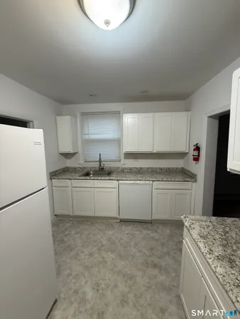 a kitchen with granite countertop a refrigerator a sink and white cabinets