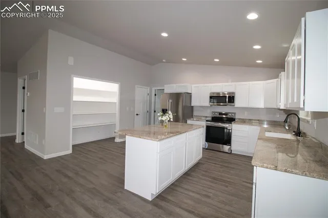 a large kitchen with kitchen island a sink a stove a refrigerator and white cabinets with wooden floor