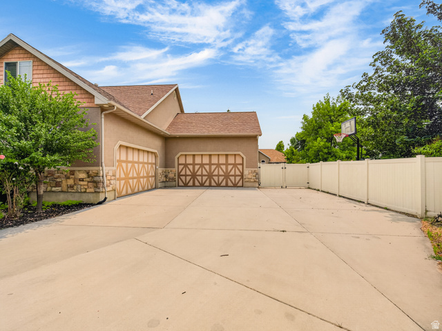 1279 West 1500th Street North Mapleton, UT 84664 - Photo 4 of 83 Expansive concrete driveway featuring a three-car garage with decorative doors, stucco and stone-veneer exterior, and a white vinyl privacy fence