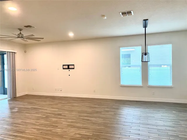 an empty room with wooden floor ceiling fan and window
