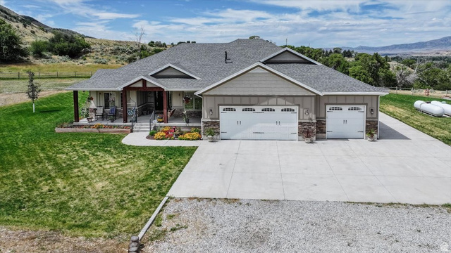 3123 East Riverdale Road Preston, ID 83263 - Photo 44 of 52 Contemporary residence featuring a covered front porch with dark wood columns, a large concrete driveway, two white garage doors with window accents, and stone façade detailing
