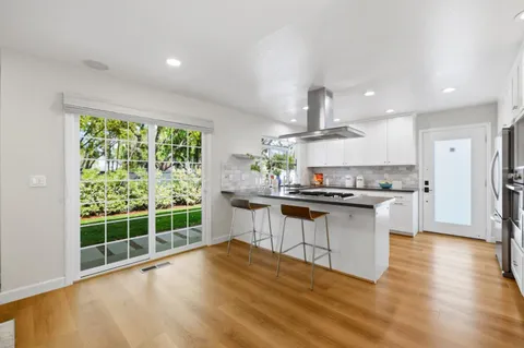 a kitchen with kitchen island granite countertop a stove a sink a refrigerator and white cabinets with wooden floor