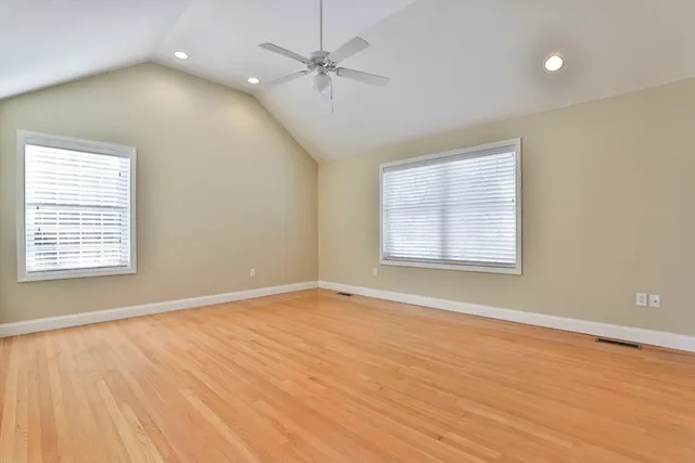 an empty room with wooden floor ceiling fan and windows