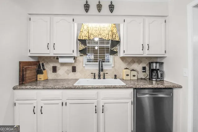 a kitchen with granite countertop a sink stainless steel appliances white cabinets and a window