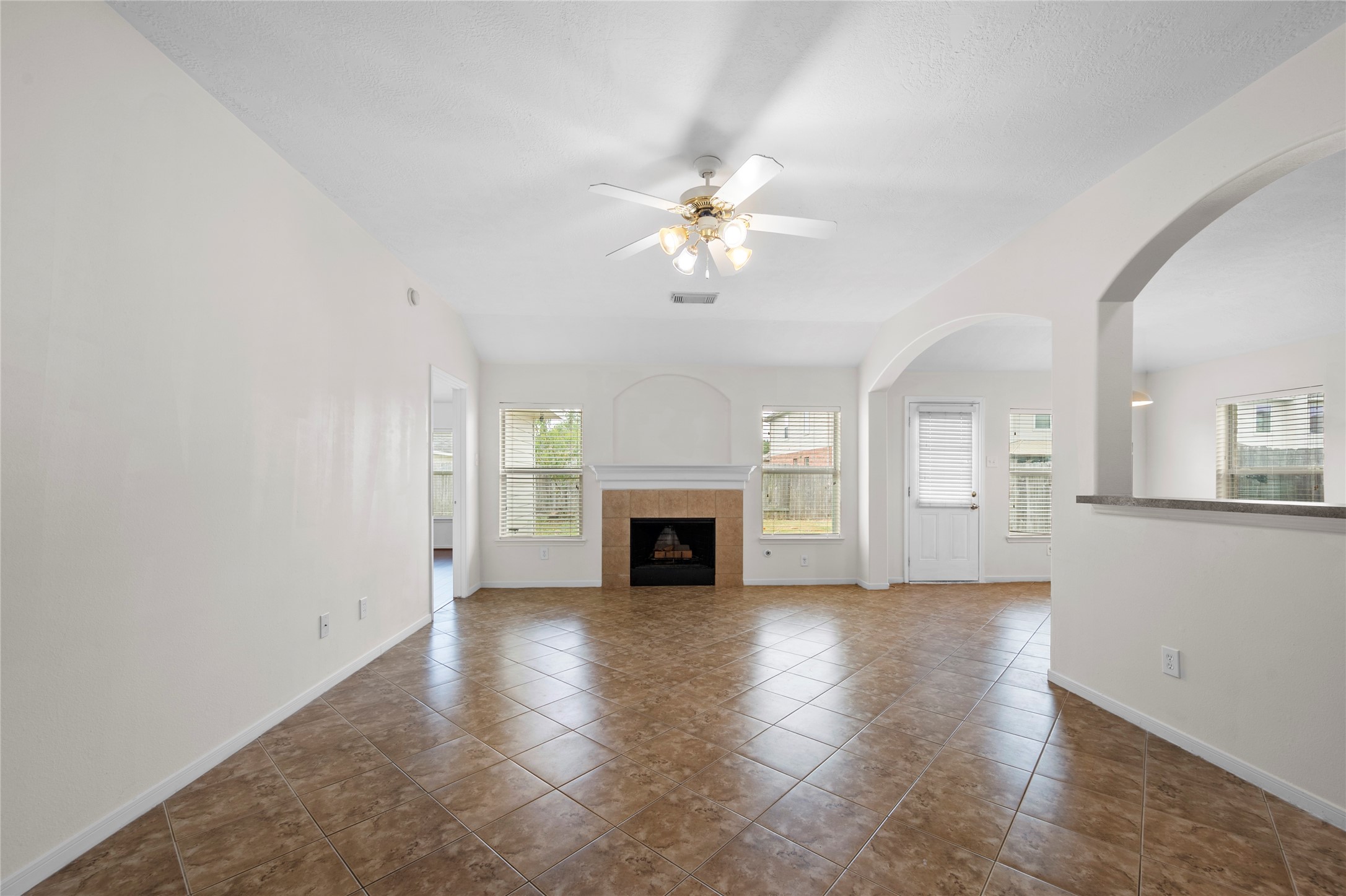 an empty room with windows fireplace and a kitchen