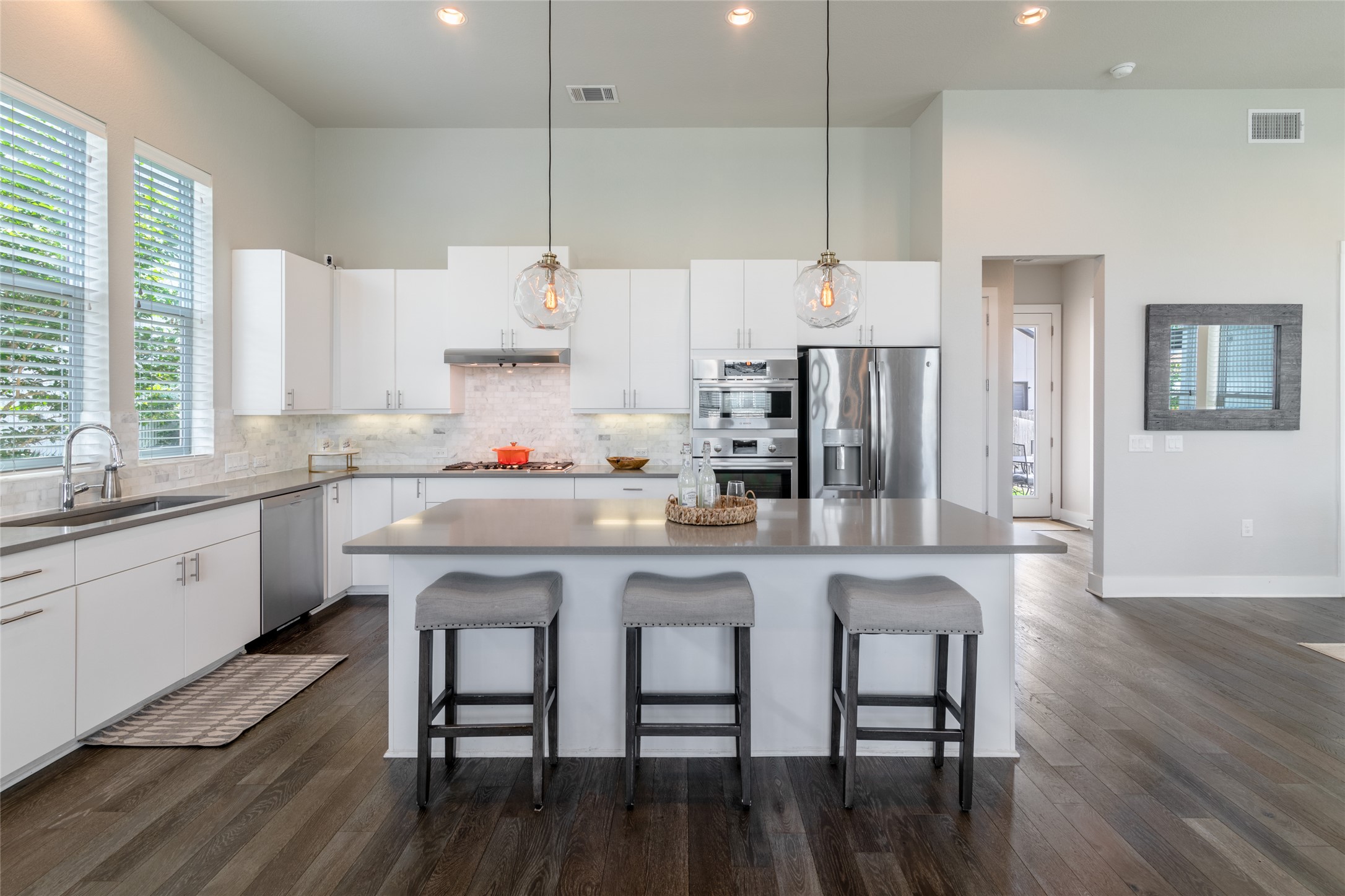 6025 Seville Drive Austin, TX 78724 - Photo 11 of 40 Contemporary kitchen featuring an oversized island with seating, white cabinetry, integrated stainless steel appliances, a tile backsplash, and dark wood-finish flooring