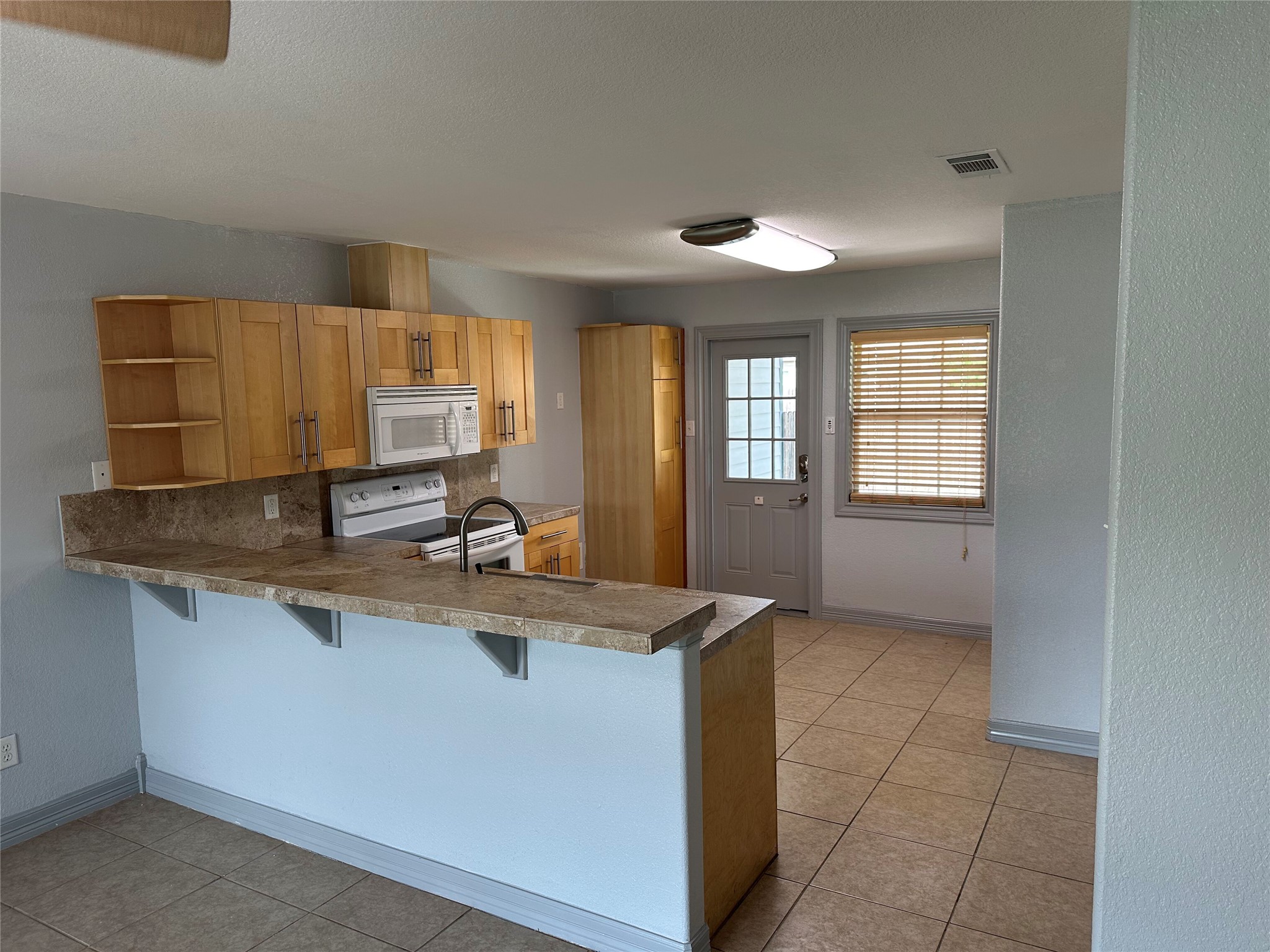 Kitchen with a kitchen bar, a peninsula, light tile patterned floors, white appliances, and a textured wall