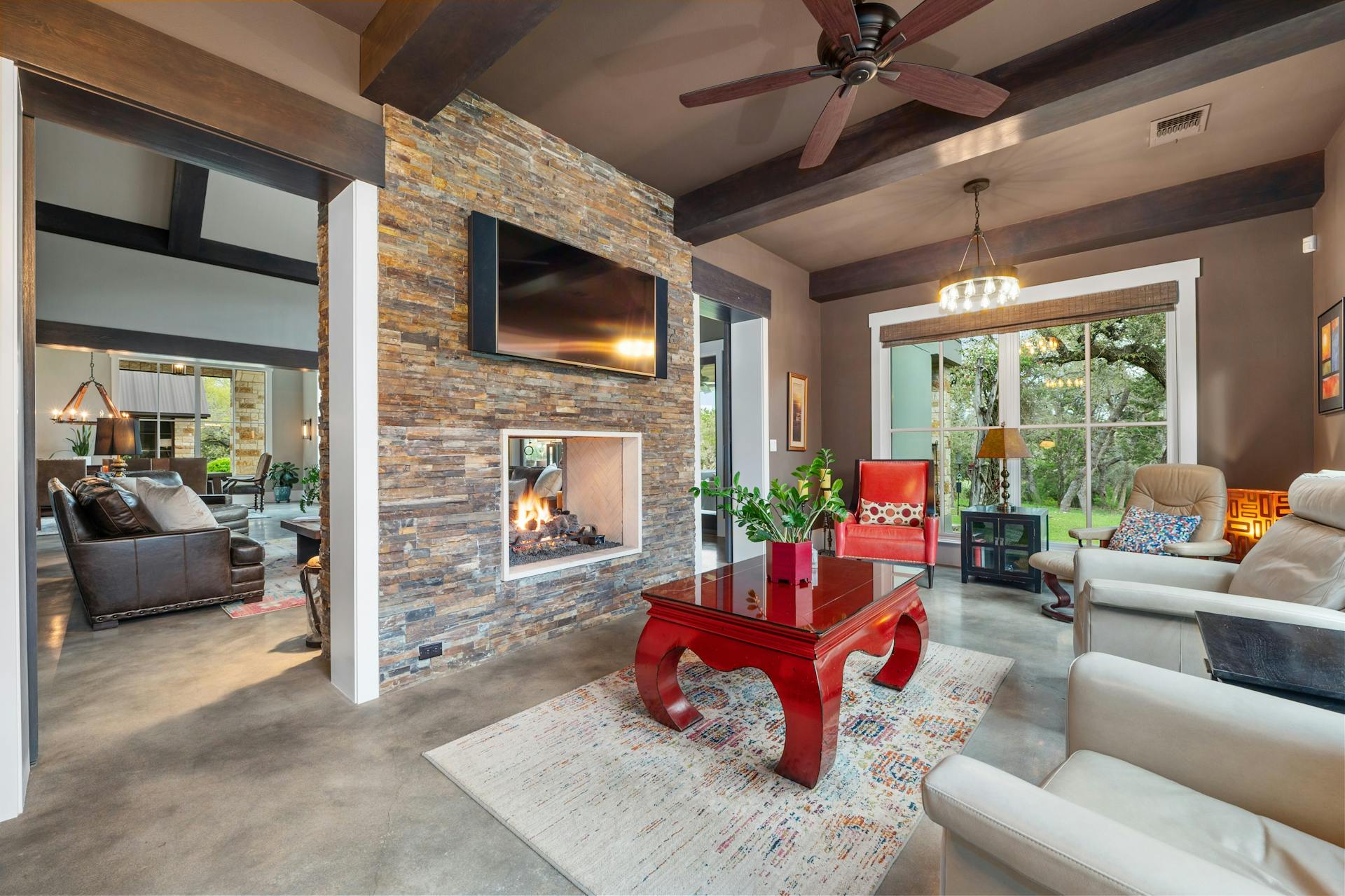 1330 Ranchers Club Lane Driftwood, TX 78619 - Photo 16 of 40 Living room featuring a ceiling fan, an outdoor stone fireplace, finished concrete flooring, hanging lights, and beamed ceiling