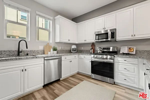 a kitchen with granite countertop white cabinets stainless steel appliances a sink and a window