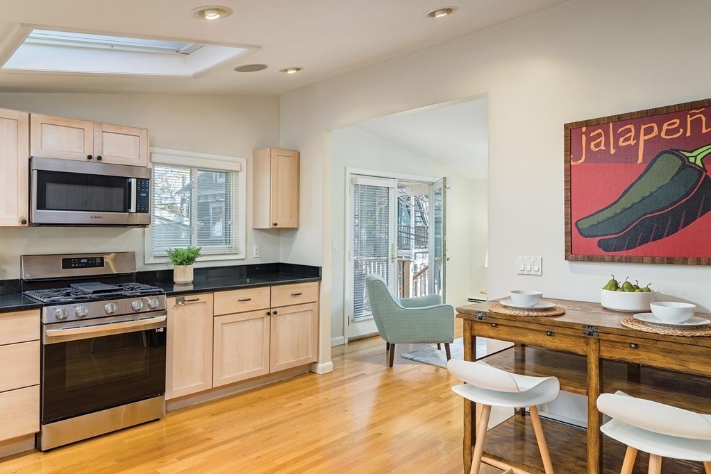 33 A Burroughs Street Boston, MA 02130 - Photo 6 of 15 a kitchen with stainless steel appliances kitchen island granite countertop a stove top oven a sink dishwasher and a dining table with wooden floor