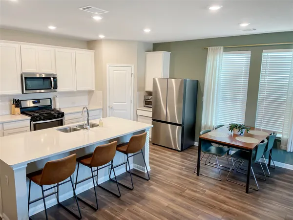a kitchen with stainless steel appliances a dining table chairs refrigerator and microwave