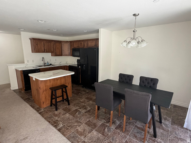 909 South Main Street, Unit F Layton, UT 84041 - Photo 3 of 20 Kitchen and dining area featuring warm wood cabinetry, a central island with a light-toned countertop, black appliances, recessed lighting, and a brushed nickel chandelier