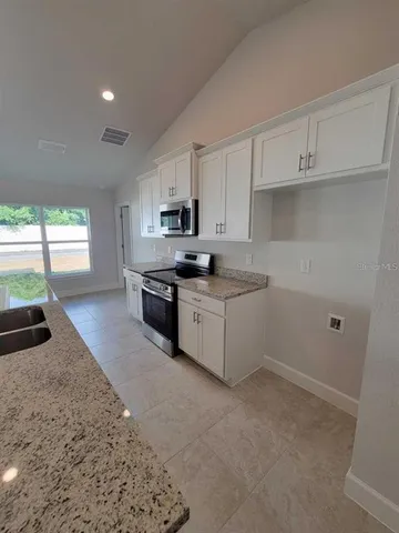 a kitchen with stainless steel appliances granite countertop a stove a sink a refrigerator white cabinets and a counter space