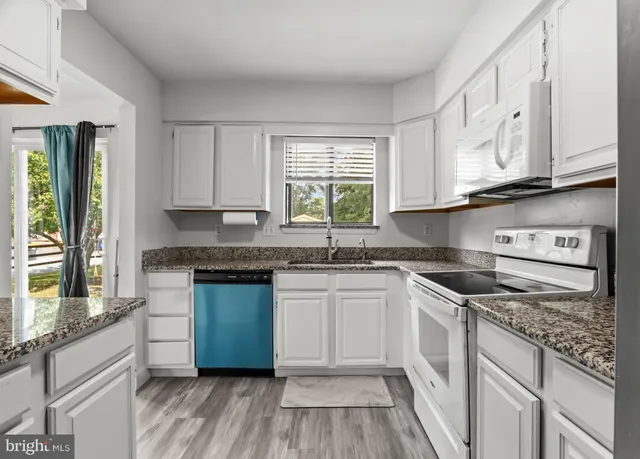 a kitchen with granite countertop wooden cabinets appliances a sink and a window