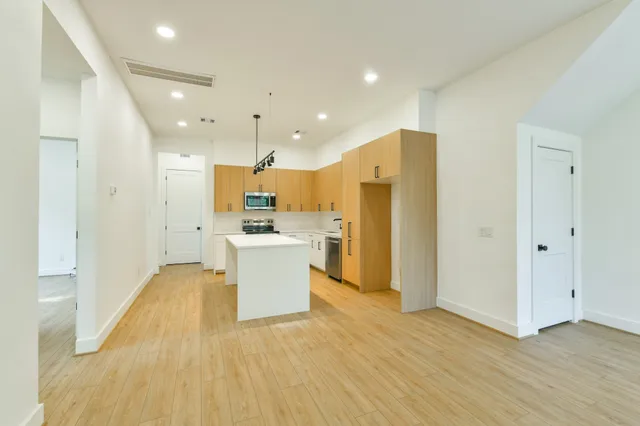 a view of kitchen with stainless steel appliances refrigerator oven and white cabinets with wooden floor