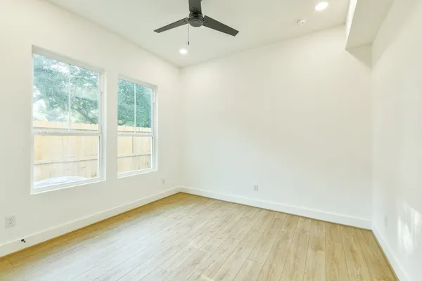 an empty room with wooden floor fan and windows