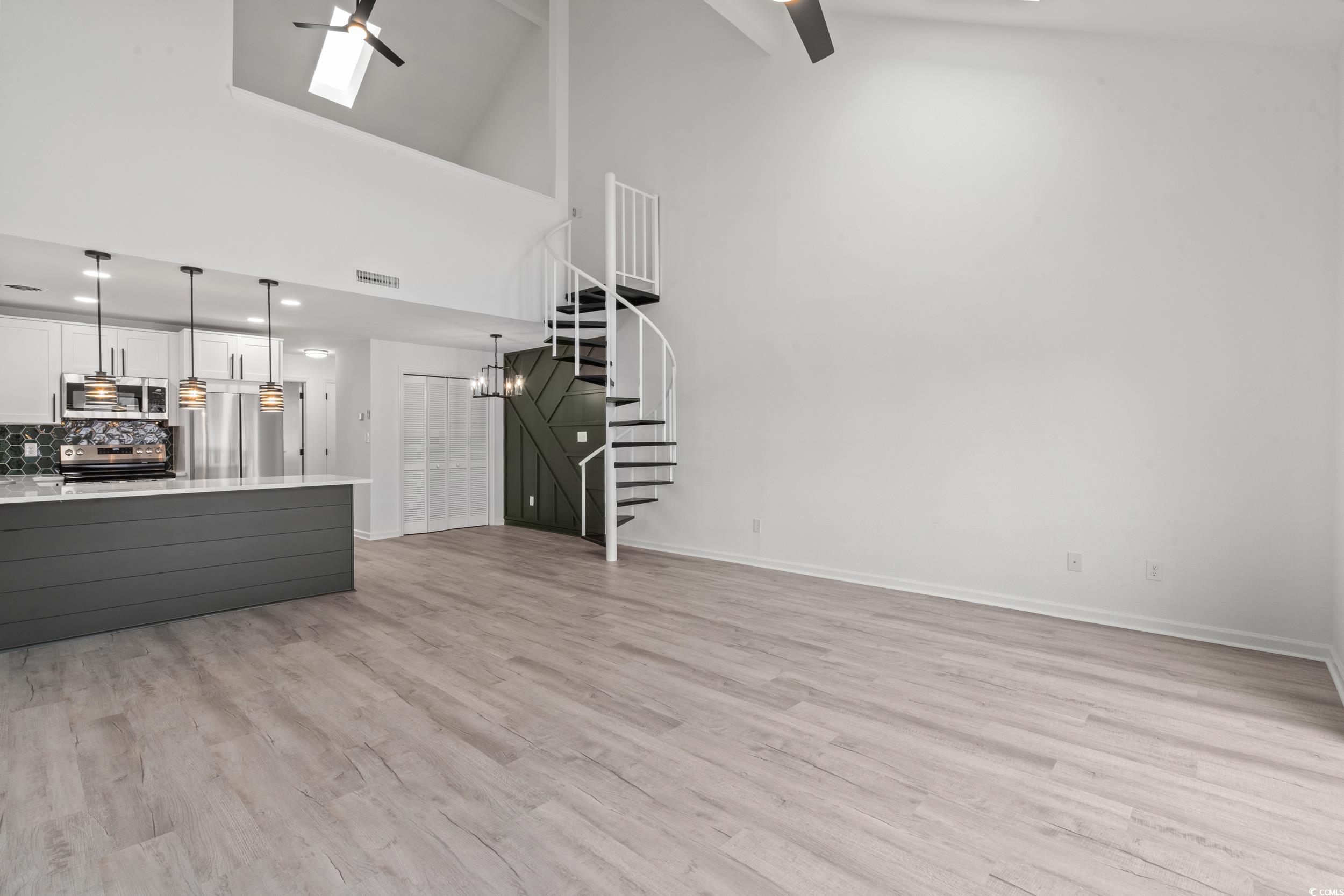 1890 Colony Drive, Unit 17L Surfside Beach, SC 29575 - Photo 15 of 38 Unfurnished living room featuring ceiling fan, stairs, light wood finished floors, a skylight, and high vaulted ceiling