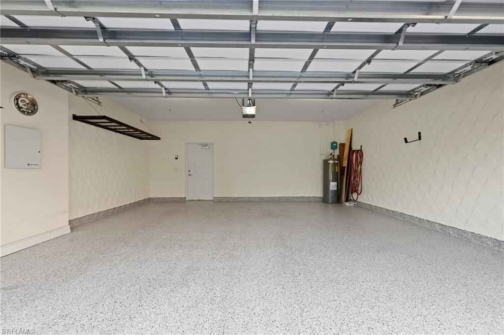 9076 Rialto Street, Unit 6204 Naples, FL 34113 - Photo 29 of 50 Spacious garage featuring a durable epoxy-finished floor, patterned wall textures, an integrated overhead storage rack, and interior door access. NEW HEAVY DUTY EPOXY FLOOR (2024), NEW HANGING STORAGE SHELVES (2021), NEW WATER HEATER (2016)