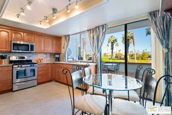 a kitchen with stainless steel appliances granite countertop a stove top oven a sink a dining table and chairs