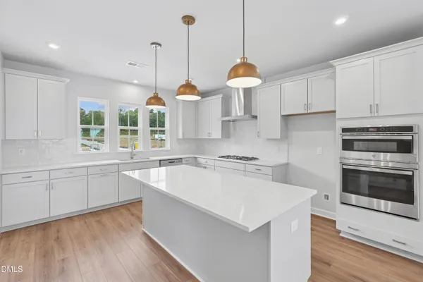 a kitchen with stainless steel appliances granite countertop a stove a sink a center island a refrigerator and a wooden floor