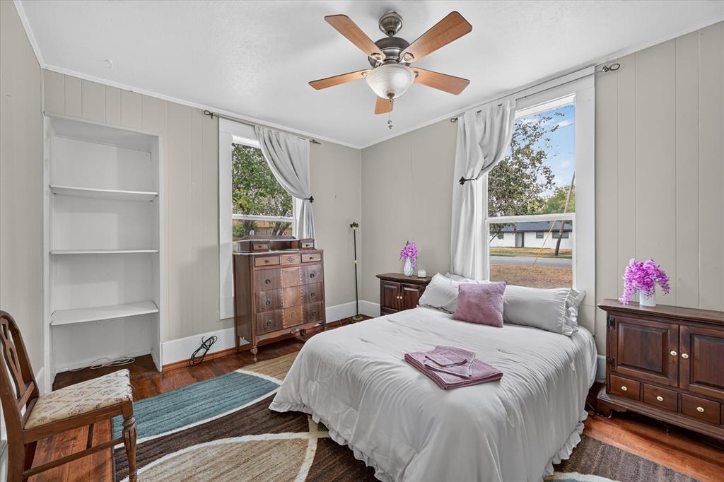 304 East Main Street Itasca, TX 76055 - Photo 26 of 38 Hardwood flooring, painted paneling, built-in shelving, ceiling fan light fixture, and two windows with white trim