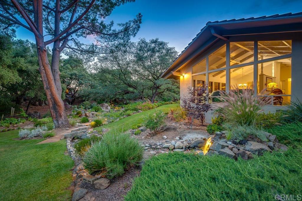a backyard of a house with plants and large tree