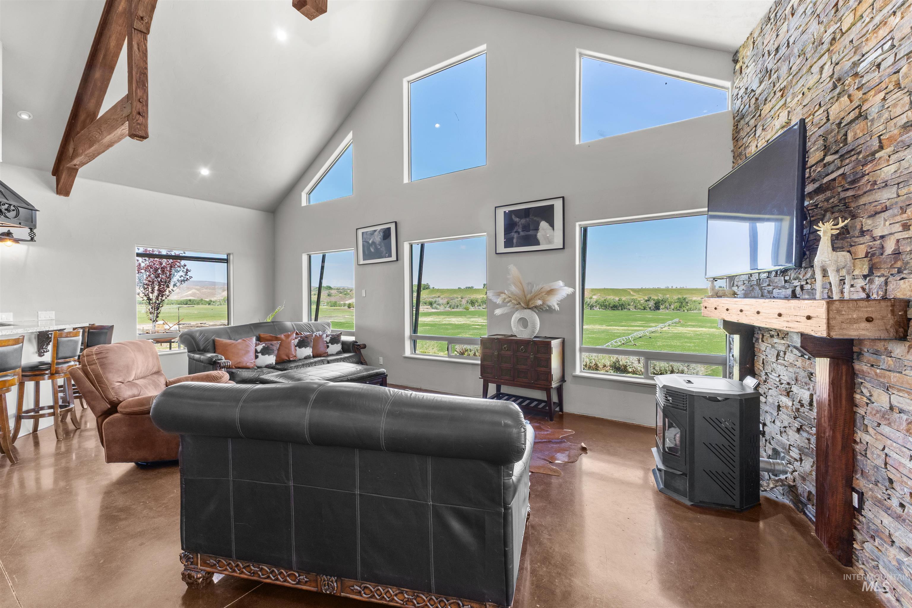 1030 Desert Glen Road Adrian, OR 97901 - Photo 30 of 47 Open-concept living space featuring a vaulted ceiling with exposed wood beams, a stacked stone accent wall with a wood mantel, and large picture windows