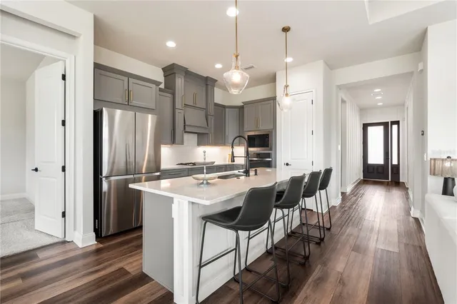 a kitchen with stainless steel appliances kitchen island granite countertop a refrigerator a oven a sink a dining table and chairs with wooden floor