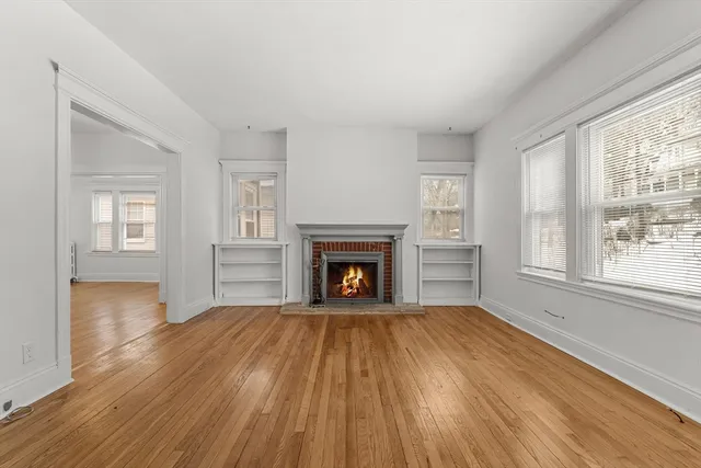 a view of an empty room with wooden floor fireplace and a window