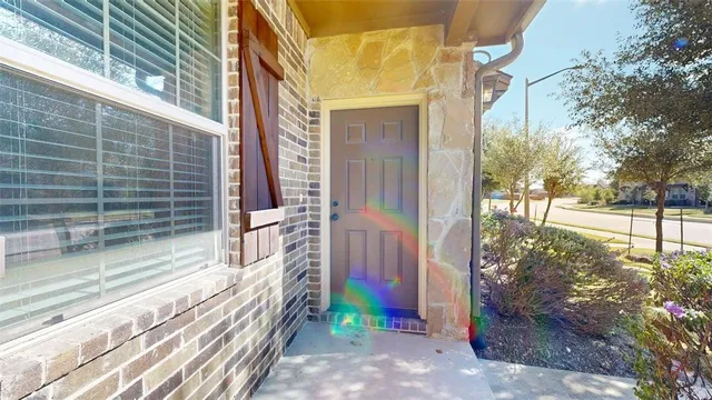 a view of a brick house with a yard plants and large tree