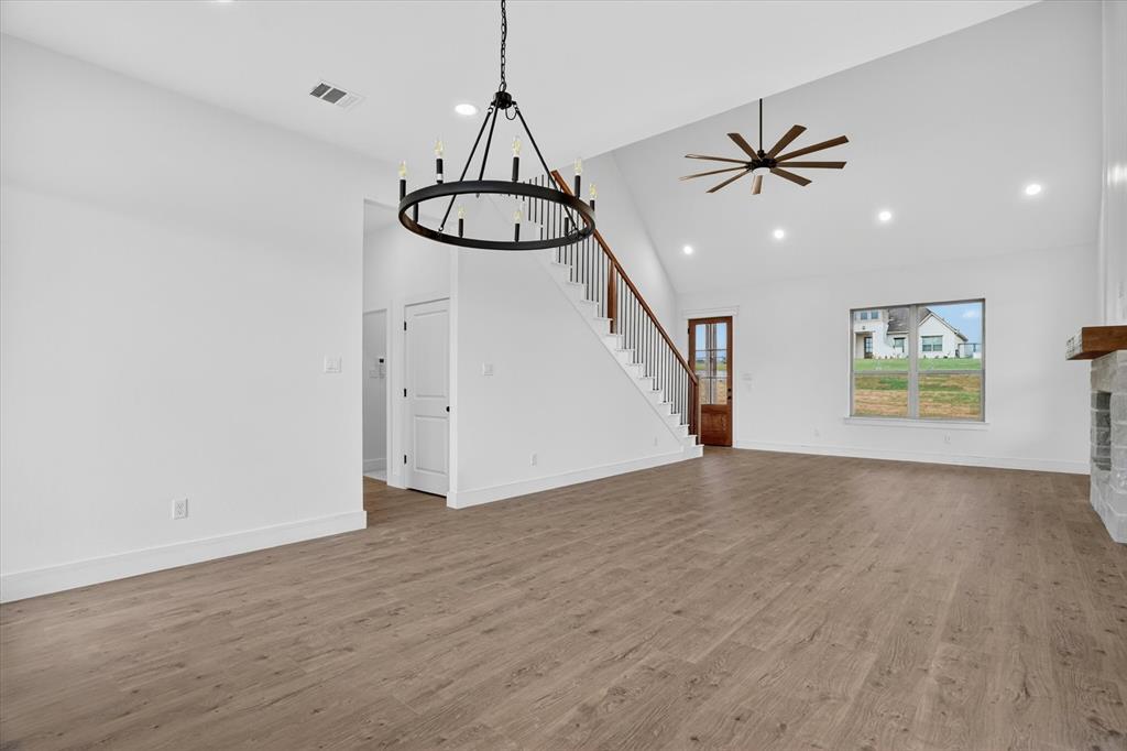 225 Kilkenny Road Poolville, TX 76487 - Photo 10 of 36 Open-concept living area featuring wood-finish flooring, a contemporary chandelier, a vaulted ceiling with a ceiling fan, a staircase with wood handrails and black balusters, and a large window