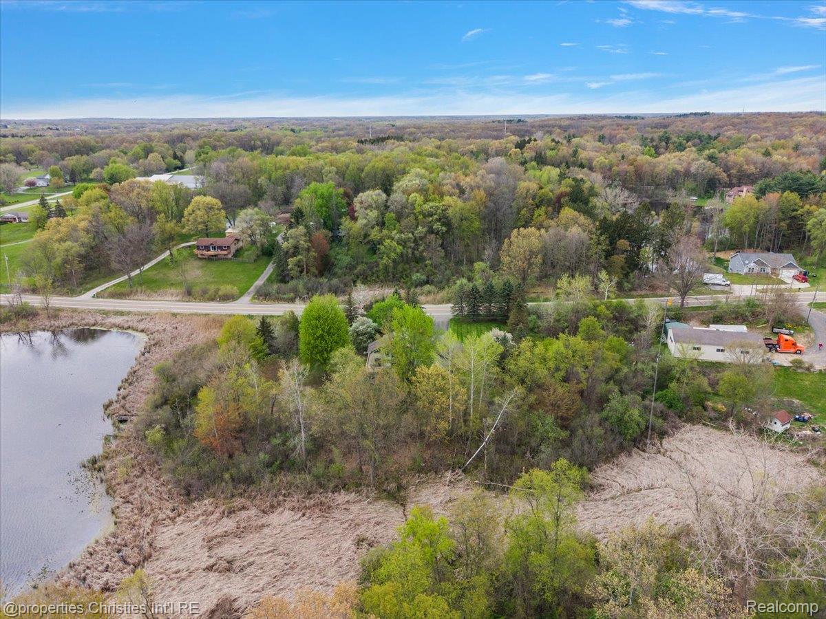 6175 Tripp Road Holly, MI 48442 - Photo 57 of 63 Aerial perspective showcasing a property surrounded by mature trees, with a water feature visible