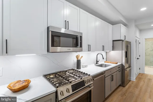 a kitchen with stainless steel appliances granite countertop a sink stove oven a refrigerator with white cabinets and wooden floor